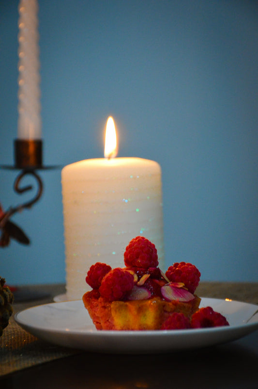 a white plate topped with a piece of cake next to a lit candle