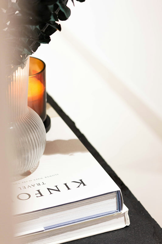 A lit candle next to a book on a surface.