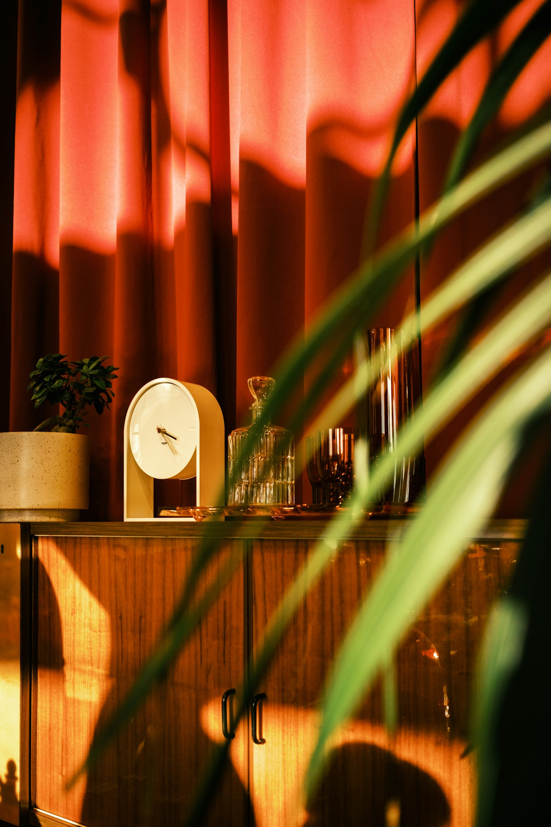 Retro cabinet with clock and plants in warm light.