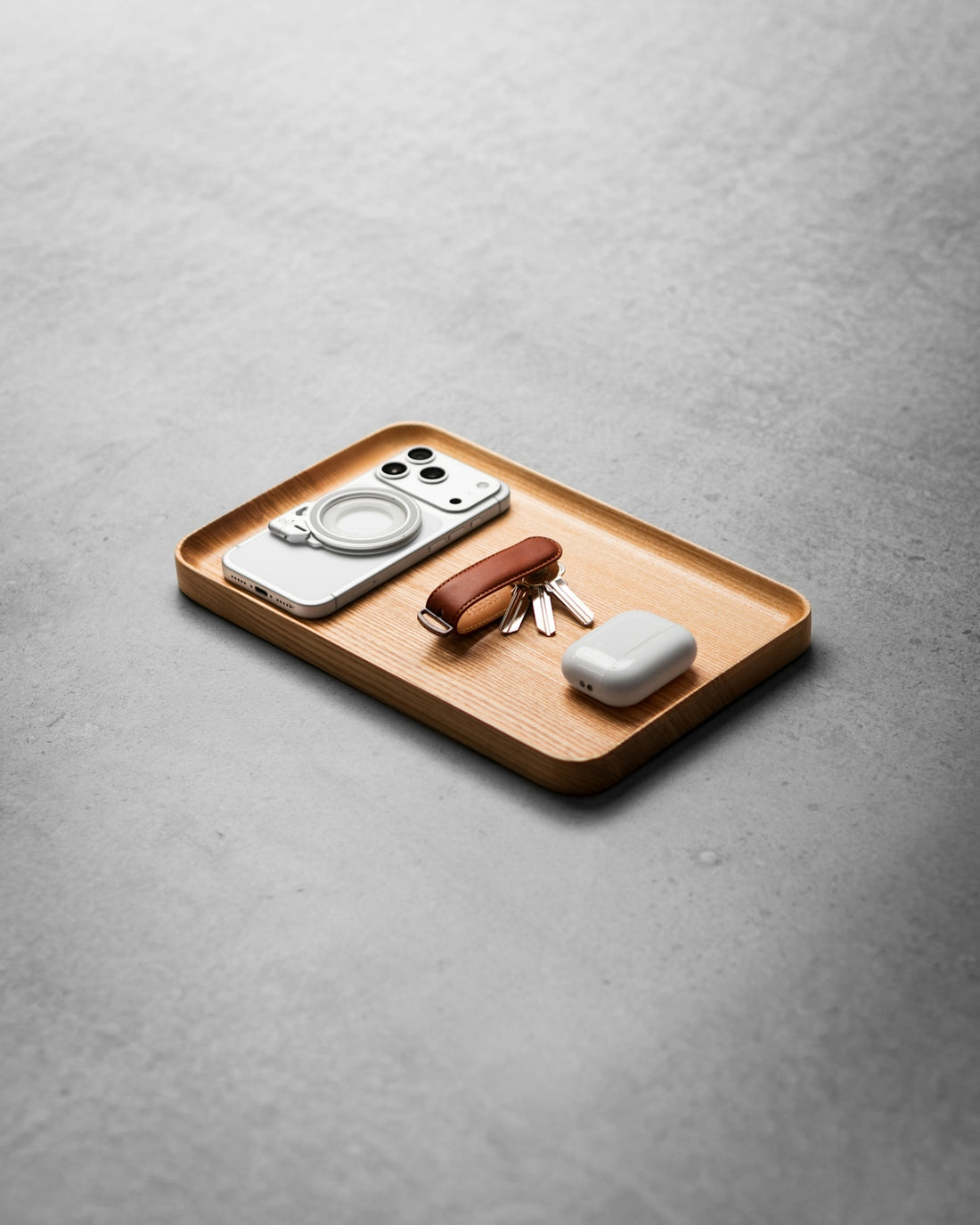 Smartphone, keys, multi-tool, and earbuds on a wooden tray.