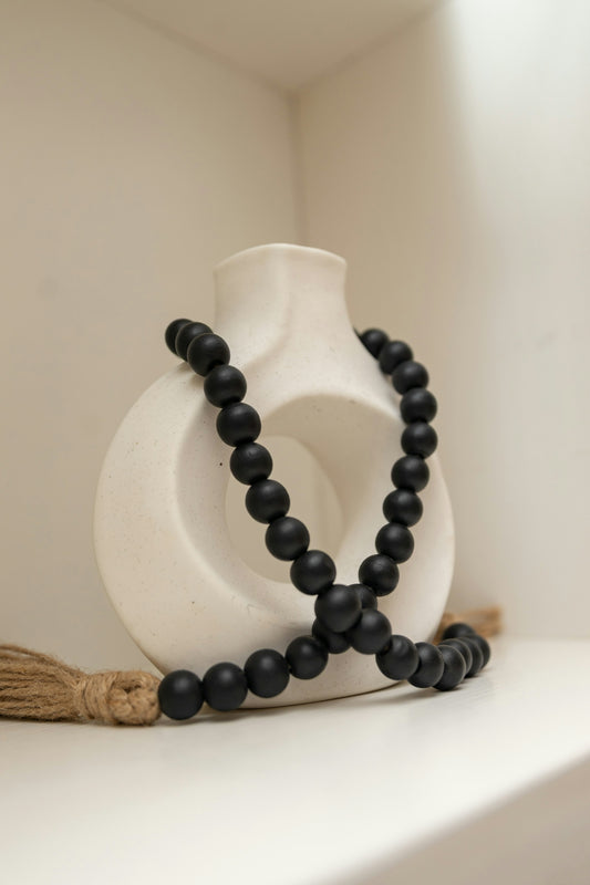 Black beaded garland draped over a white abstract vase.
