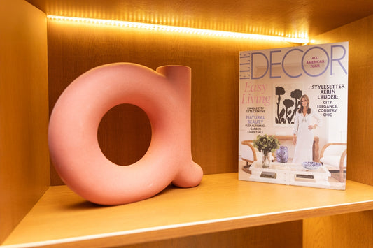 Pink 'a' decor and magazine on a lit wooden shelf.