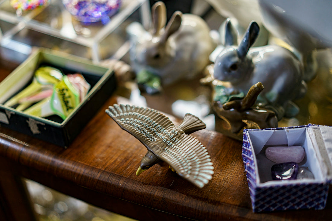 A ceramic bird figurine with spread wings on a wooden surface near rabbit statues