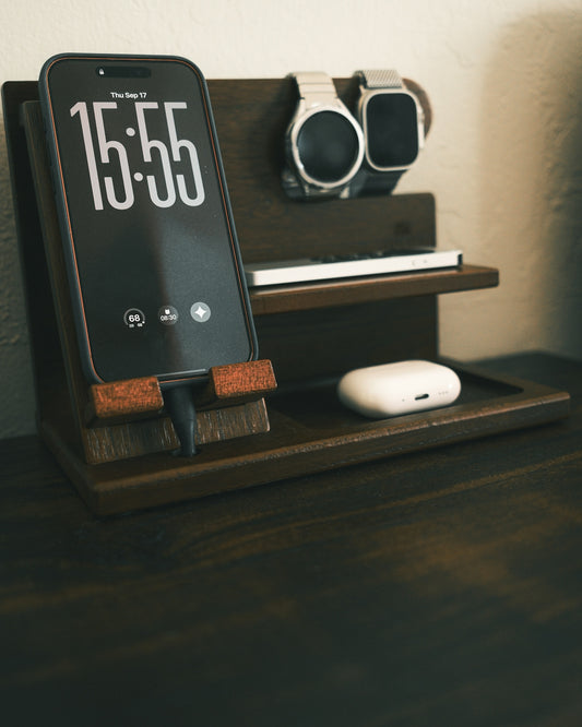 A smartphone, two smartwatches, and wireless earbuds on a wooden charging station